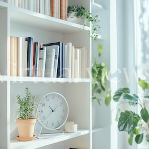 Bright white bookshelf styled with neutral-toned books, lush green houseplants, and a minimalist round clock. Positioned by a sunlit window, this serene setup is perfect for enhancing any living space with a touch of nature and modern elegance.