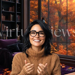 May include: A woman with dark hair wearing glasses and a brown sweater smiles at the camera. She is sitting in a room with a large window overlooking a forest with fall foliage. The room has a dark wood bookcase filled with books and a purple armchair.