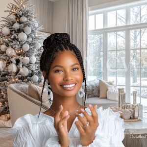 May include: A woman with long black braids smiles while wearing a white blouse and a silver necklace. She is standing in front of a Christmas tree decorated with white baubles and a large window with a snowy view.