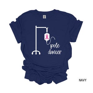 May include: Navy blue t-shirt with a white graphic of an IV pole and the text "pole dancer". The IV bag has a pink ribbon.