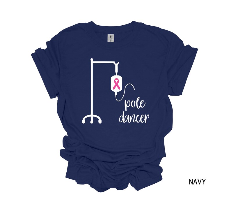 May include: Navy blue t-shirt with a white graphic of an IV pole and the text "pole dancer". The IV bag has a pink ribbon.