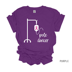 May include: Purple t-shirt with a white graphic of an IV pole with a pink ribbon and the text "pole dancer".