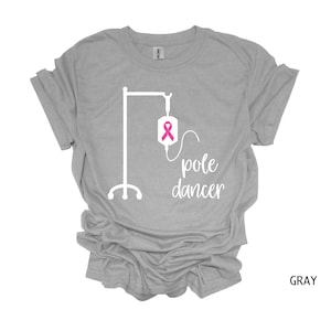 May include: Gray t-shirt with a white graphic of an IV bag with a pink ribbon and the text "pole dancer".