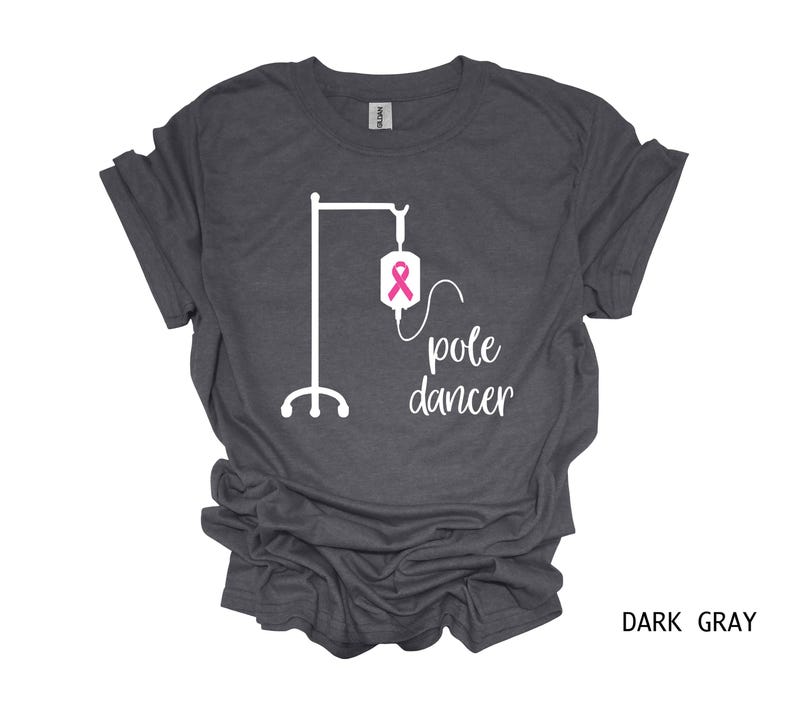 May include: Dark gray t-shirt with a white graphic of an IV pole and the text "pole dancer". The IV bag has a pink ribbon.