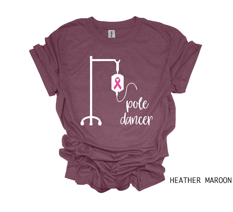 May include: Heather maroon t-shirt with a white graphic of an IV pole and the text "pole dancer". The IV bag has a pink ribbon.