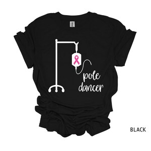 May include: Black t-shirt with a white graphic of an IV pole and the text "pole dancer". A pink ribbon is on the IV bag.