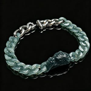 May include: A bracelet featuring a combination of translucent pale green resin chain links and a metallic silver-toned chain section. The piece includes a detailed, dark green sculpted dragon head charm integrated into the chain design with a clasp.