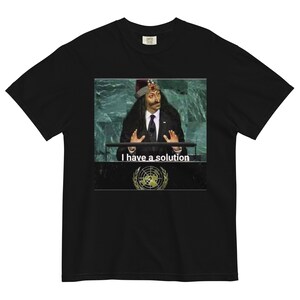 Könnte beinhalten: Schwarzes T-Shirt mit einem Foto eines Mannes in einem roten Hut und Anzug, der an einem Podium spricht. Der Text "I have a solution" ist unter dem Foto gedruckt.