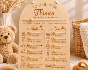 May include: An arched light wood daily routine board with engraved French text and icons. It features sliding wooden beads on horizontal cords to track tasks for morning and evening, plus a day of the week tracker at the top labeled La routine de Thiméo.