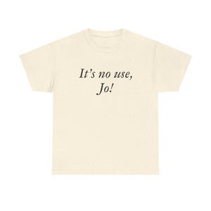 May include: Cream-colored t-shirt with the text "It's no use, Jo!" in a black, elegant font. The shirt has a classic crew neck and short sleeves, suitable for casual wear. The fabric appears to be a soft, comfortable material.