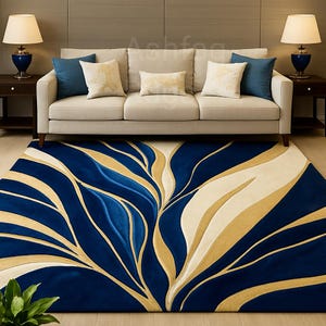 Può includere: Un grande tappeto con un sorprendente design astratto in blu navy, crema e oro. Il tappeto presenta un motivo fluido e organico che ricorda foglie stilizzate o correnti d'acqua. Un divano beige con cuscini blu e crema è sopra.