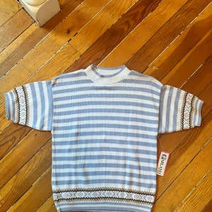 May include: A blue and white striped short-sleeved sweater with a brown and white patterned trim. The sweater has a mock neck and is made of a soft, knitted fabric. The sweater has a tag that says "Charland" on it.