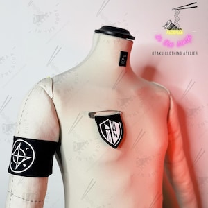 Könnte beinhalten: Eine weiße Schaufensterpuppe trägt eine schwarze Armbinde mit einem weißen Symbol. Die Puppe trägt einen schwarz-weißen Aufnäher mit dem Text "NEENA IN THE SOUP" auf der Brust. Der Hintergrund ist ein rosa Farbverlauf mit dem Text "neena in the soup OTAKU CLOTHING ATELIER" in Neonrosa.