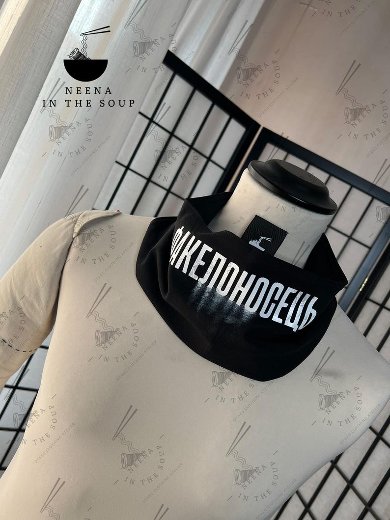 May include: Black neck gaiter with white Cyrillic text. The gaiter is displayed on a mannequin. The brand logo "NEENA IN THE SOUP" is visible in the background.