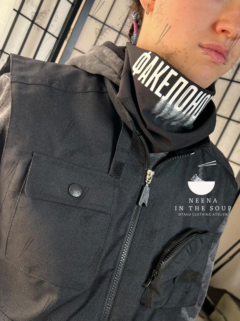 May include: Black vest with multiple pockets and a zipper closure. The vest has a button on the pocket and a small zipper pocket. A black neck gaiter with white text is visible. The text on the neck gaiter reads "FAKEПОНЧИ". The vest is part of the "Neena in the Soup" otaku clothing atelier.