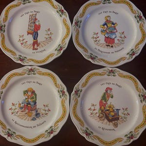 May include: A set of four white ceramic plates with scalloped edges, featuring colorful illustrations of historical street vendors titled Les Cris de Paris. Each plate depicts a different worker with text including Le Vitrier, La Marchande de Poissons, Le Raccommodeur de Faïence, and Le Rétameur, surrounded by a yellow and green floral border.