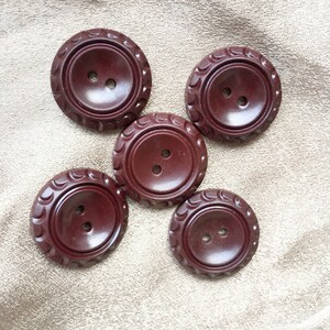 May include: Five brown plastic buttons with two holes each. The buttons have a decorative, scalloped edge.