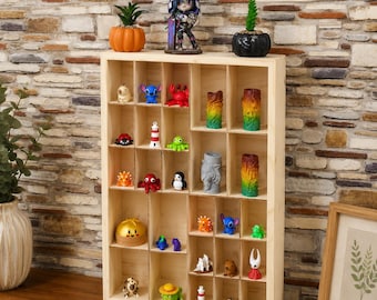 May include: A rectangular light-colored wooden display shelf with multiple square compartments. The shelf contains various small colorful plastic figurines, including animals, lighthouses, and abstract shapes, arranged across the grid-like structure.