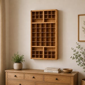 Peut inclure: Une vitrine murale rectangulaire en bois dotée d'une grille composée de nombreuses petites cases carrées. L'unité est fabriquée en bois brun clair avec une finition au grain naturel, conçue pour organiser et présenter de petits objets.