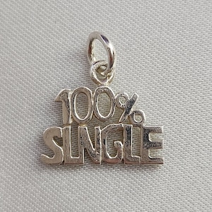 May include: A silver charm pendant with the words "100% SINGLE" in bold, capital letters. The pendant has a small loop at the top for attaching to a necklace or bracelet. The charm is displayed against a light gray background.