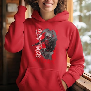 May include: A red hoodie with a graphic print of a female anime character with a mask and pigtails holding a sword. The character is standing in front of a white background with black kanji characters.