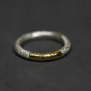 May include: A silver ring with a gold band around the center. The ring has a textured surface.