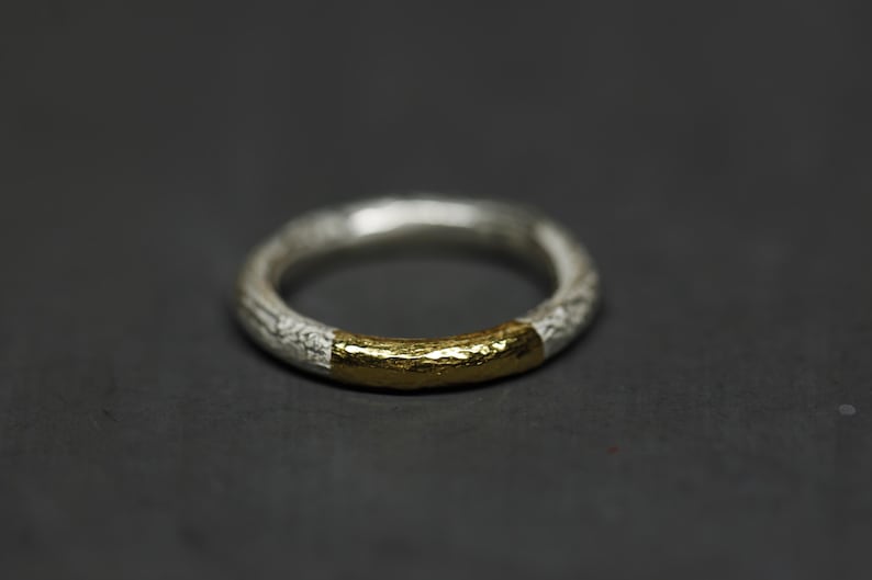 May include: A silver ring with a gold band around the center. The ring has a textured surface.