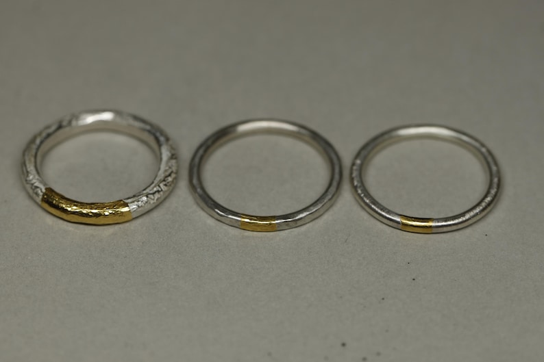 May include: Three silver rings with a thin gold band around each ring.