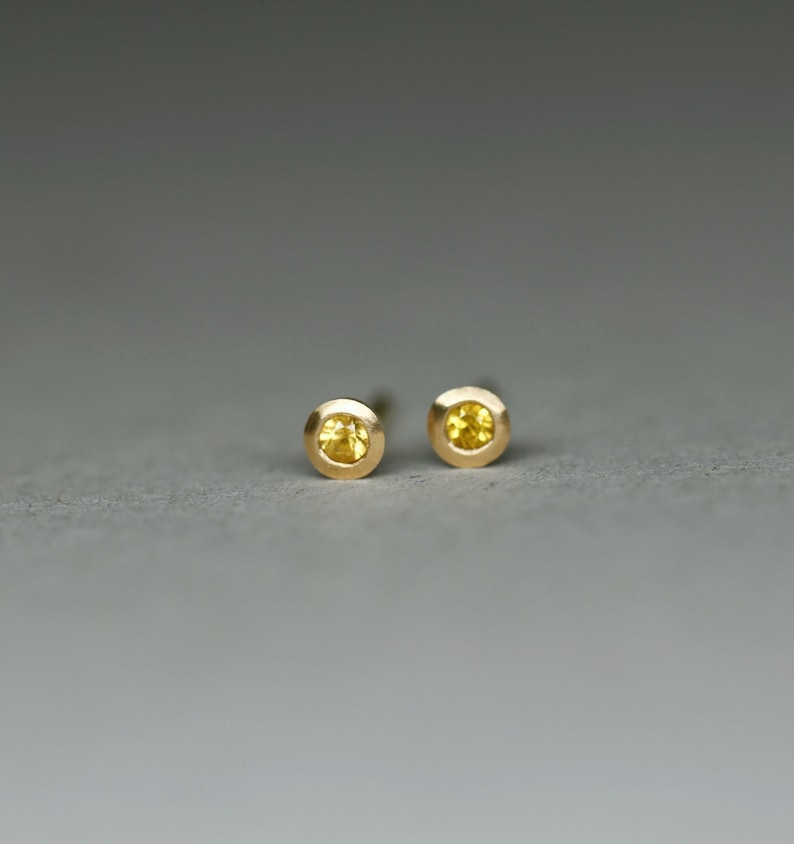 K&ouml;nnte beinhalten: Ein Paar goldene Ohrstecker mit kleinen gelben Edelsteinen.