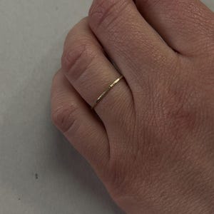 May include: A thin gold band ring with a hammered texture.