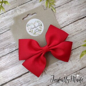 May include: A red hair bow with a white circle sticker that says "Handmade with love".