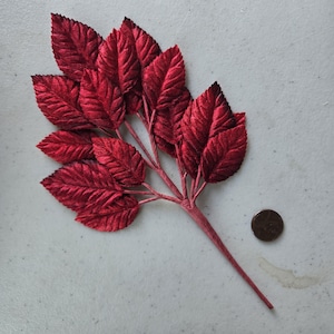 May include: A sprig of artificial red velvet leaves with a long stem. The leaves are arranged in a cluster and have a slightly textured surface.