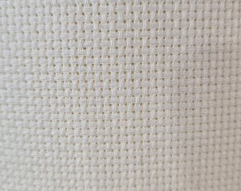 May include: Close-up of a cream-colored fabric with a woven texture. The fabric has a grid-like pattern created by the interwoven threads. The texture appears soft and slightly raised, with small holes.