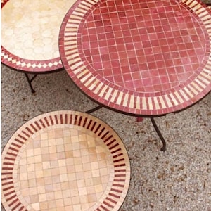 May include: Three round tables with mosaic tile tops. One table features a deep red center with a cream and red border. Two tables feature cream-colored centers with red and cream borders. Each table has thin, dark metal legs and a circular frame.