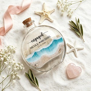 Peut inclure: Une bouteille en verre transparent avec un bouchon en liège contenant du sable et un motif de vague océanique en résine bleue. Le verre porte le texte noir engaged, NICOLE AND MICHAEL, et 03.16.2026. La bouteille est entourée d'étoiles de mer.