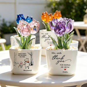 Peut inclure: Plusieurs arrangements floraux de tulipes décoratives dans des pots en céramique blancs. Les tulipes sont en verre coloré, notamment rose, violet, orange et bleu. Les pots portent des inscriptions de remerciement.
