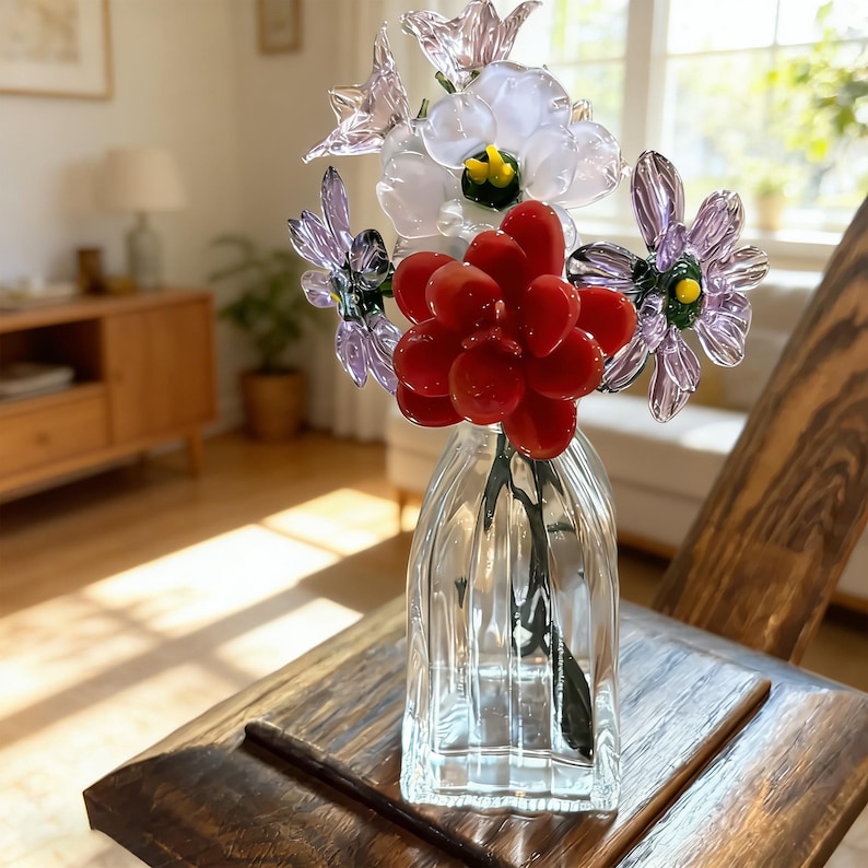May include: A glass vase holding a colorful glass flower arrangement. The arrangement includes red, purple, and white flowers. The vase is clear and sits on a wooden surface.