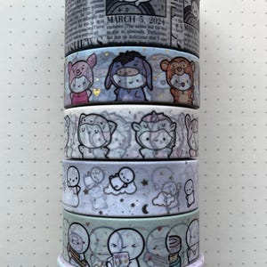 Puede incluir: Una pila de rollos de cinta adhesiva decorativa con varios diseños. Los rollos presentan ilustraciones de personajes de dibujos animados, nubes y el texto "MARCH 5, 2024". La paleta de colores incluye pasteles, plata y blanco.