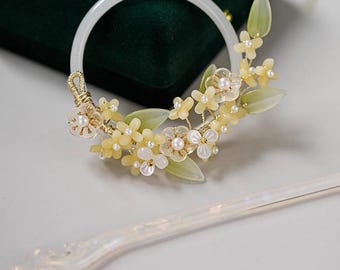 May include: A white hair accessory set featuring a circular headband and a decorative hair stick. The headband is adorned with yellow flowers, pearls, and green leaves. The hair stick has a pearlescent finish with a dangling charm.