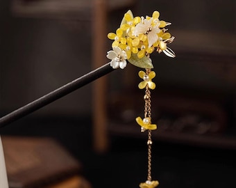May include: A decorative hair stick featuring a cluster of yellow and white flowers with pearl accents. The flowers are attached to a dark wooden stick, with a delicate chain of yellow flowers dangling below.