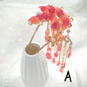 May include: A decorative hair accessory featuring a floral design with red and orange petals, pearls, and gold accents. The hairpiece is held in a white vase. The letter "A" is visible on the plate.