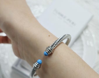 May include: A silver bangle bracelet with a twisted design and two turquoise blue stones on the ends.