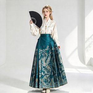Può includere: Una camicetta color crema a maniche lunghe con scollo a V e una gonna lunga color ottanio a vita alta con intricati ricami dorati e bianchi raffiguranti fenici e nuvole. Un ventaglio pieghevole nero e una lunga collana con pendente.