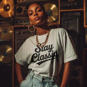 Peut inclure: Une personne porte un t-shirt blanc avec l'inscription "Stay Classic" en noir. La personne porte des bijoux dorés et un jean bleu clair. L'arrière-plan présente du matériel audio vintage et des disques vinyles dorés.