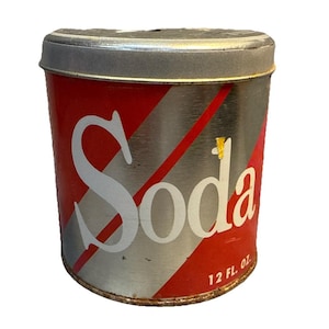 May include: A vintage soda can with a silver and red design. The word "Soda" is prominently displayed in white, with a diagonal red stripe. The can is 12 fl. oz. and has a silver lid.