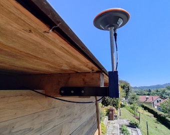 May include: A GPS receiver mounted on a wooden structure. The receiver has a gray and orange dome and is attached to a black bracket. The wooden structure is made of light brown planks, and the sky is blue.