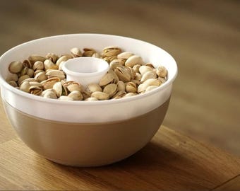 May include: A white and brown ceramic bowl filled with pistachios. The bowl has a removable center piece.