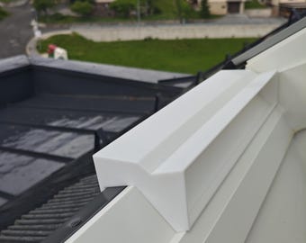May include: A white, V-shaped plastic component mounted onto the edge of a window frame. The piece features a smooth, matte finish with a distinct angular profile designed to fit securely over the top of the window structure.