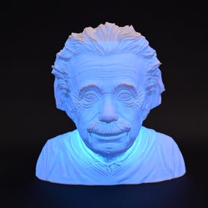 Könnte beinhalten: Weiße Büste von Albert Einstein mit einem blauen Licht, das von innen leuchtet. Die Skulptur ist aus glattem, weißem Material gefertigt und zeigt Einsteins ikonische Frisur und seinen Schnurrbart.