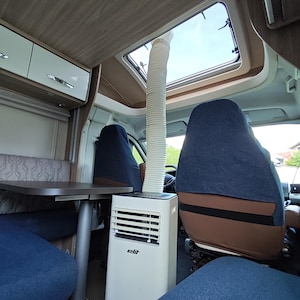 May include: A white portable air conditioner with the brand name elit printed on the front, positioned inside a vehicle cabin. A flexible white exhaust hose extends from the top of the unit upward through an open rectangular roof vent.